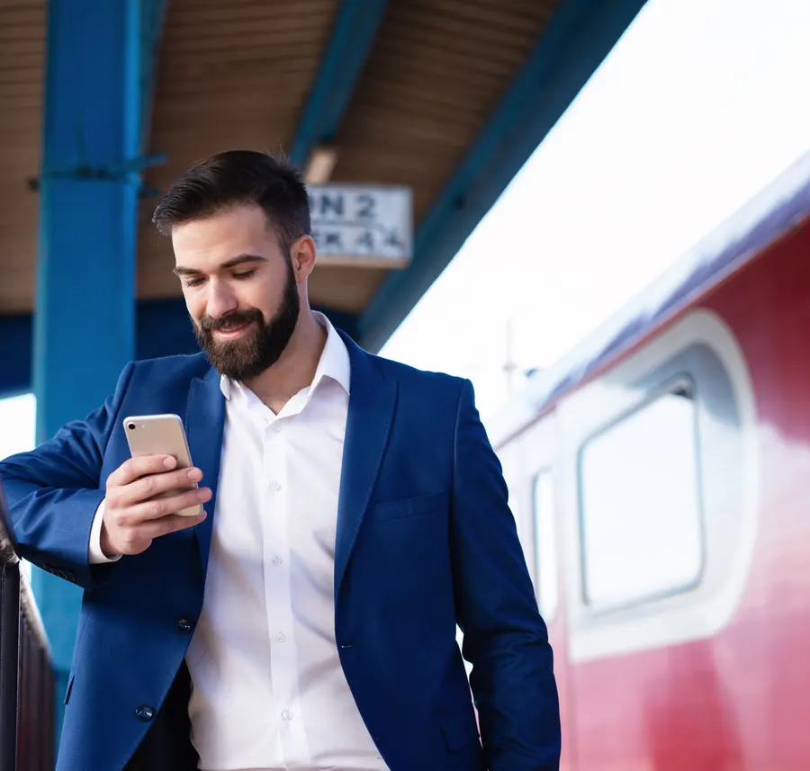 Un futur agent en costume révise sur son téléphone, sur le quai d'une gare